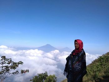 Woman wearing hijab standing on mountain against blue sky