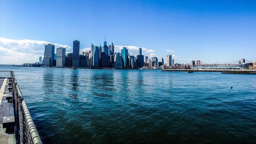 Sea by modern buildings against blue sky