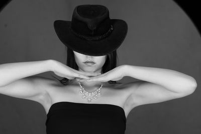 B/w portrait of young woman eyes and nose covered by a black hat, hands forming a wave below cheek