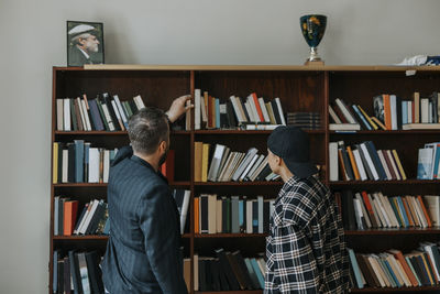 Mature male professor reaching for book while standing by student in library