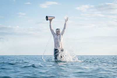 Rear view of man jumping in sea against sky