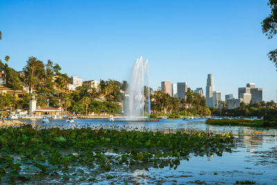 Fountain by lake and buildings against clear sky echo park