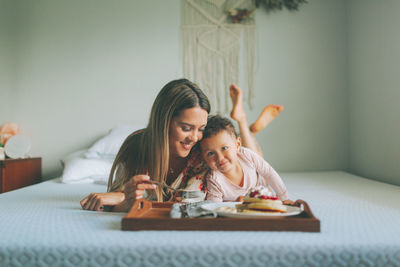 Mother and daughter eating food on bed at home