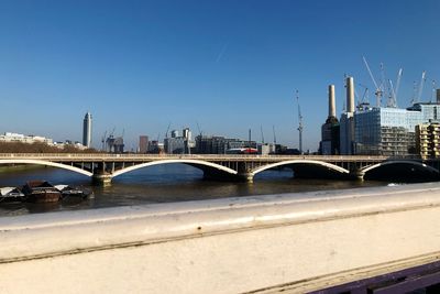 Bridge over river in city against clear blue sky