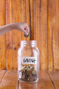 Close-up of child putting coin in jar on table