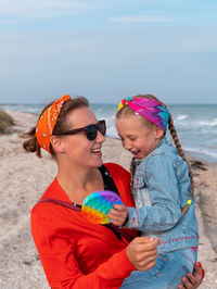 Cheerful mother daughter smiling walking on beach happy family cute child playing rainbow pop it toy