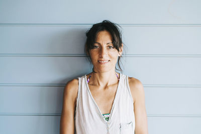 Portrait of smiling young woman standing against wall