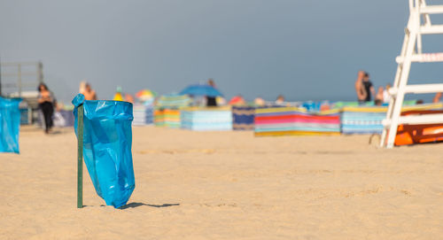 An empty garbage bag on the beach on a sunny summer day, in the background people, a beach screen