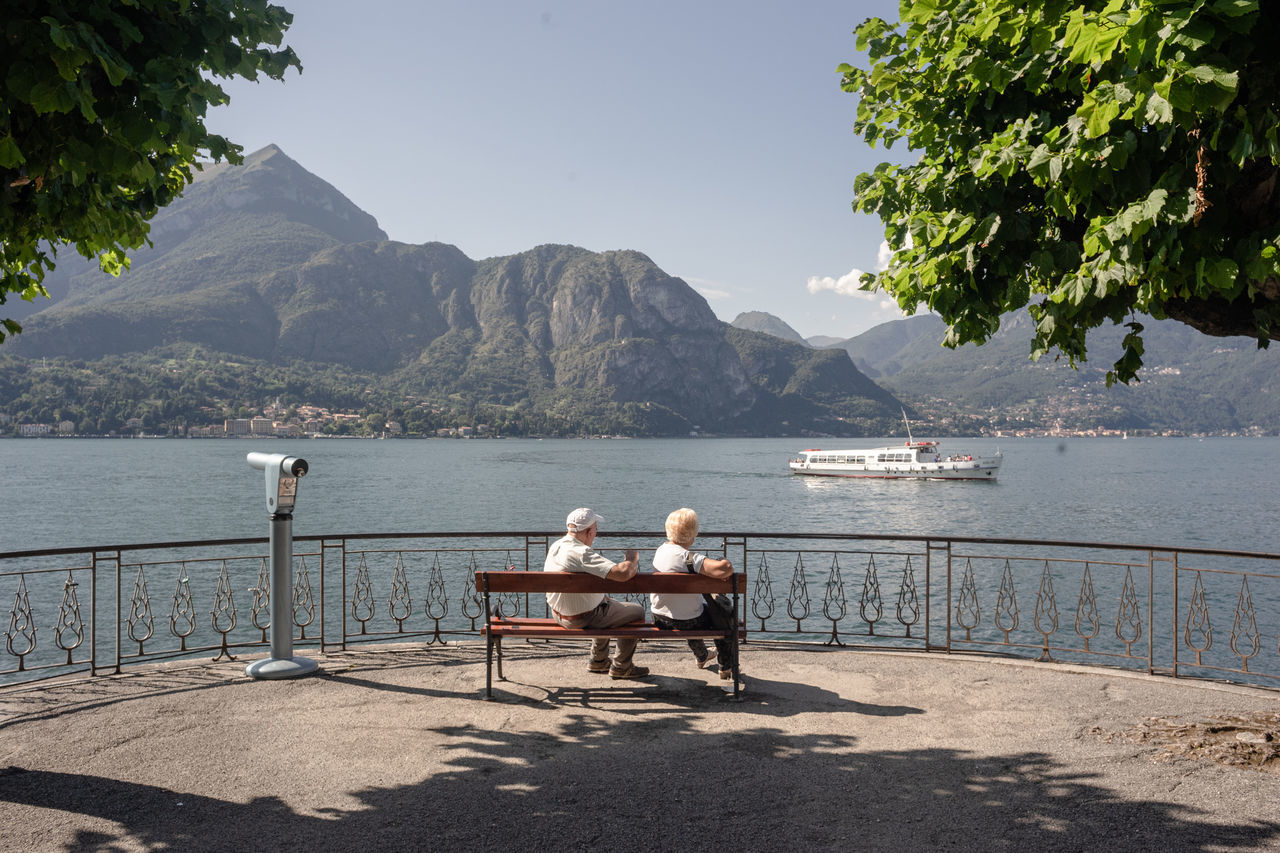 water, mountain, nature, sky, real people, beauty in nature, sea, women, two people, day, nautical vessel, adult, men, sitting, bench, seat, plant, scenics - nature, transportation, outdoors, couple - relationship