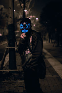 Portrait of the unknown man behind the neon mask on street at night. dark brown tone