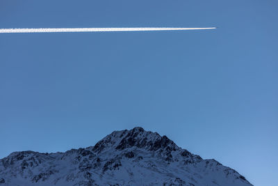 Vapor trail over european alps against clear blue sky