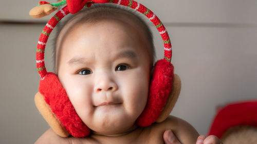 Cropped image of hands holding cute baby boy wearing ear muff against wall