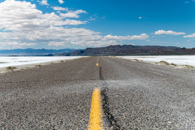 Lower angle of an empty road with some mountains on the horizon surrounded by salt flat land. 