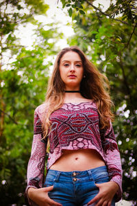 Low angle portrait of beautiful young woman standing against trees