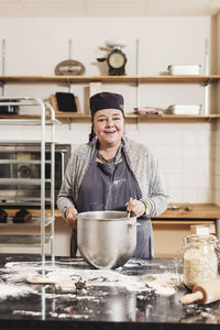 Portrait of smiling mature baker cooking by kitchen counter