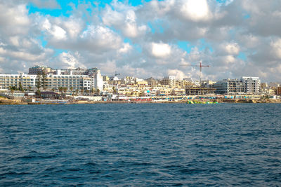 Sea by buildings against sky in city