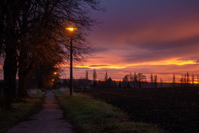 Street amidst field against sky during sunset