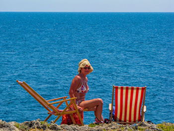 Man sitting on chair by sea against sky