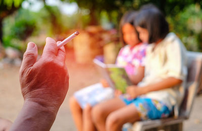 Cropped hand holding cigarette with girls in background