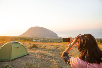 Woman takes photos of the sunrise in the mountains on her phone. selfie in rising sun. panoramic 