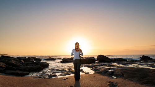 Rear view of man standing on beach at sunset