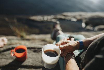 Woman sitting on rock and drinking coffee at lakeshore