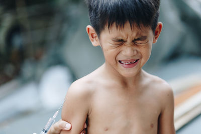 Cropped hand injecting syringe to scared boy