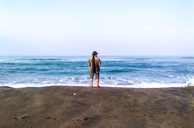 Rear view of man standing on beach against sky