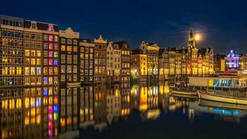 Damrak in amsterdam with the moon and old houses during the bluehour in the netherlands 