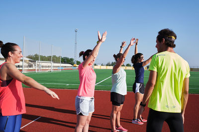 Group of women practice pre-workout stretching with their young traine