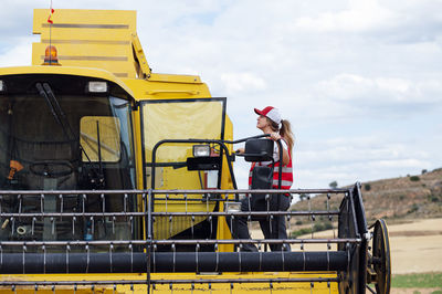 Full body side view of female worker in uniform getting into industrial combine harvester while working in agricultural field