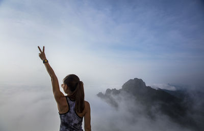 Rear view of woman with hand raised standing against sky