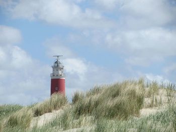 Lighthouse on field against cloudy sky