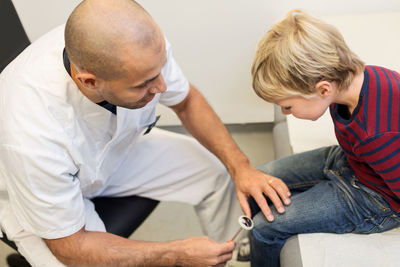Male orthopedist checking knee reflexes of boy at clinic
