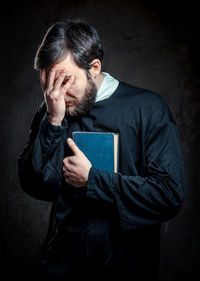 Portrait of priest with bible with face in hand