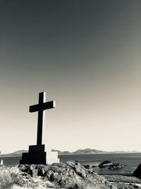 Cross on rock against clear sky during sunset