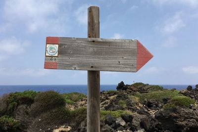 Sign board on shore against sky