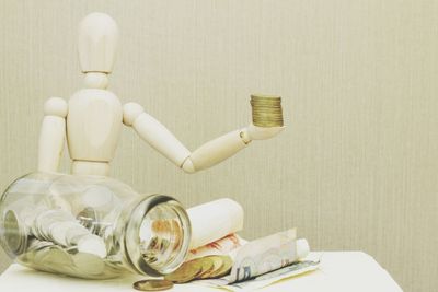 Wooden figurine with jar and coins on table against wall