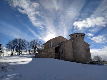 Snow covered field by building against sky