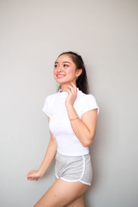 Portrait of a smiling young woman standing against white wall