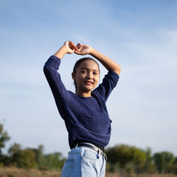 Low angle portrait of teenager girl standing against sky