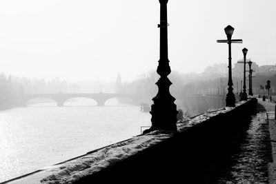 Gas lights by river against clear sky during foggy weather