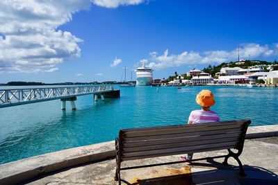 Rear view of woman sitting on bench by sea against sky