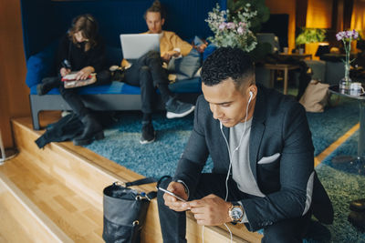 Businessman listening to in-ear headphones sitting at office cafeteria