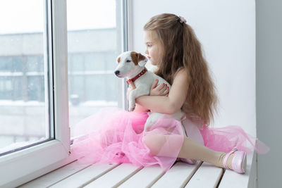 Rear view of woman with dog sitting on pink indoors