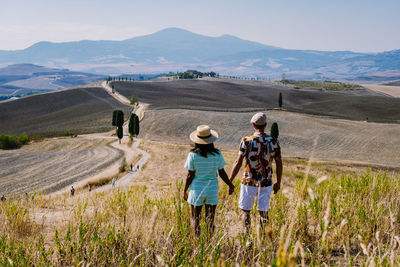 Rear view of people walking on field against mountains