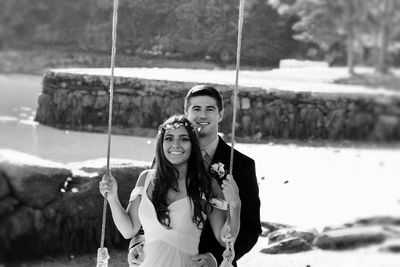 Portrait of groom standing behind bride on swing at park