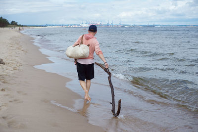 Rear view of friends on shore at beach against sky