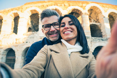 Portrait of couple doing selfie while standing against historical building
