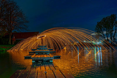 Illuminated ferris wheel by lake against sky at night